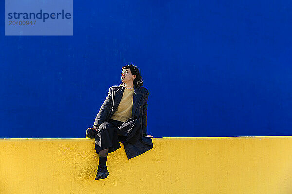 Woman in casuals sitting on top of yellow wall