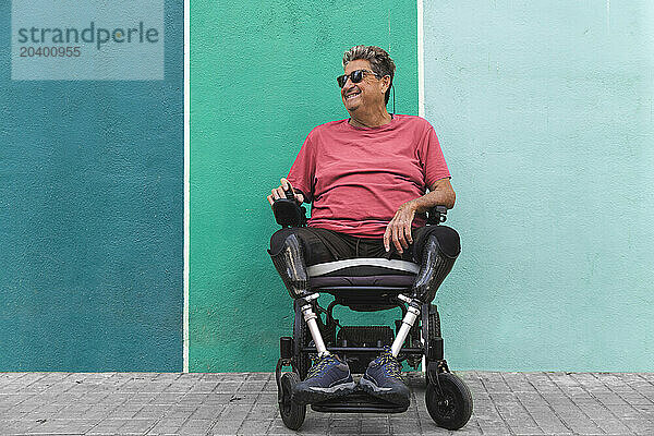 Smiling senior man in motorized wheelchair in front of green wall