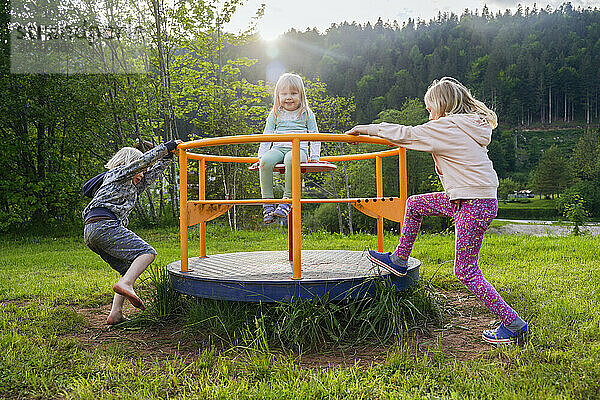 Siblings spinning and enjoying carousel at playground