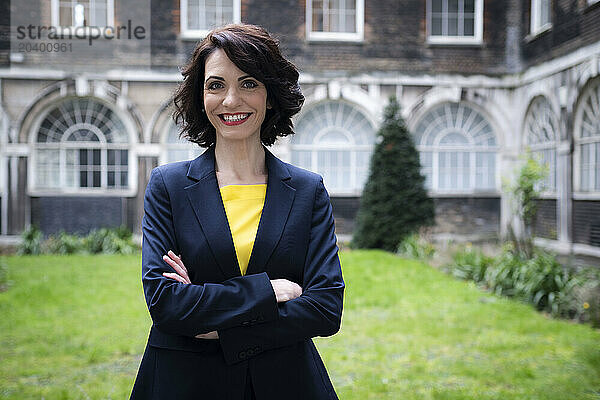 Smiling businesswoman standing with arms crossed at office park