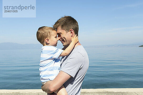 Father embracing son in arms at sea on sunny day