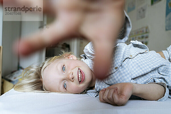 Happy boy wearing pajamas and showing stop gesture on bed at home