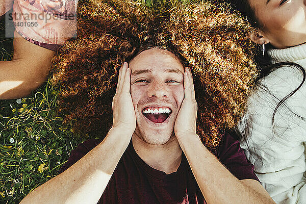 Happy man with curly hair lying down on grass at park