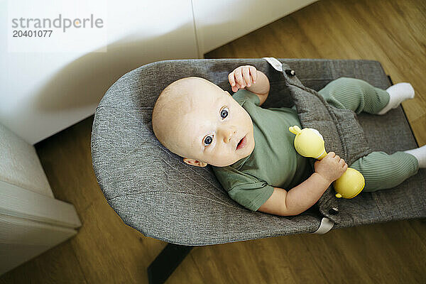 Cute baby boy and holding yellow toy sitting in rocking chair