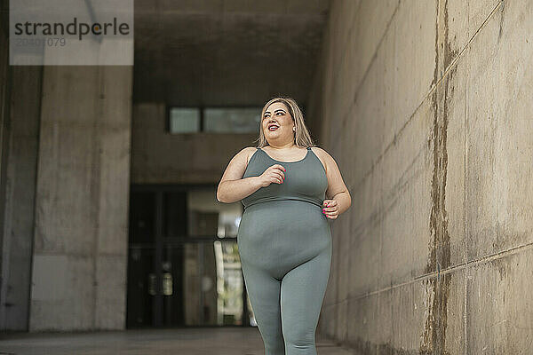 Happy curvy woman running near wall