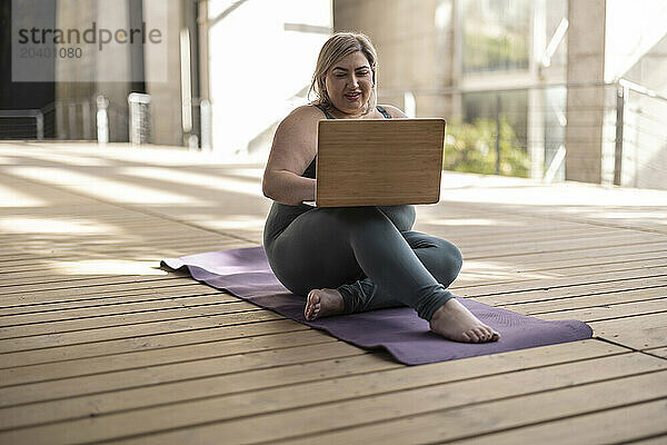 Smiling curvy woman using laptop on mat