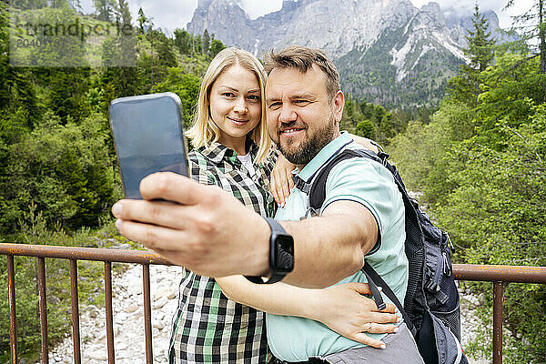 Smiling man taking selfie with woman in front of Dolomites