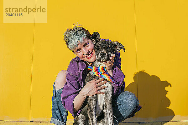 Smiling lesbian woman crouching near dog with multi colored bandana around neck