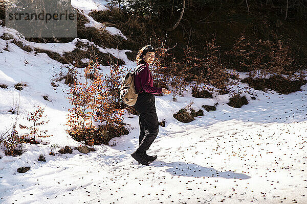 Smiling woman walking on snowy footpath in winter forest