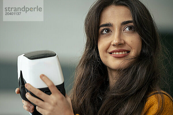 Smiling woman holding virtual reality headset and contemplating at home