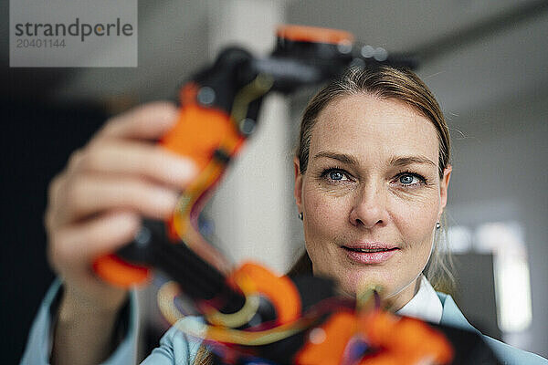 Smiling engineer examining robotic arm at office