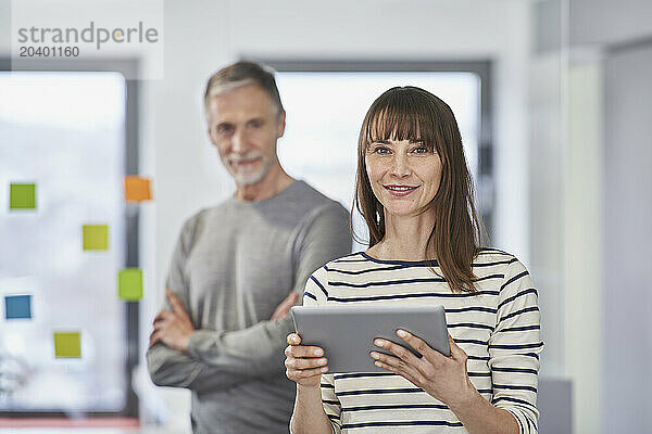 Businesswoman holding tablet PC in office with colleague at workplace