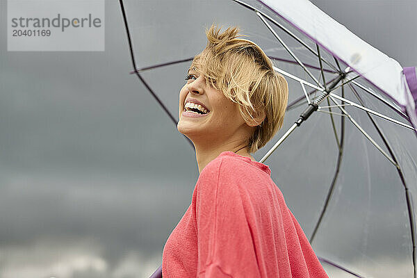 Cheerful young blond woman with umbrella on rainy day