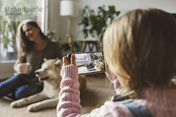 Girl photographing grandmother and dog through smart phone at home