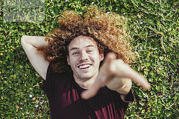 Smiling man with hand behind head lying on grass at park