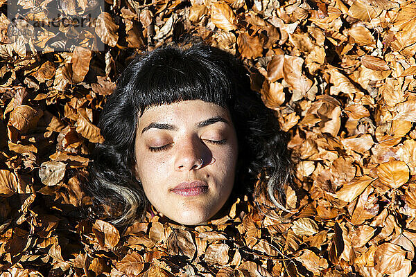 Woman with eyes closed amidst fallen autumn leaves