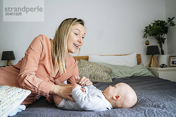 Smiling blond mother playing with toddler son lying on bed at home