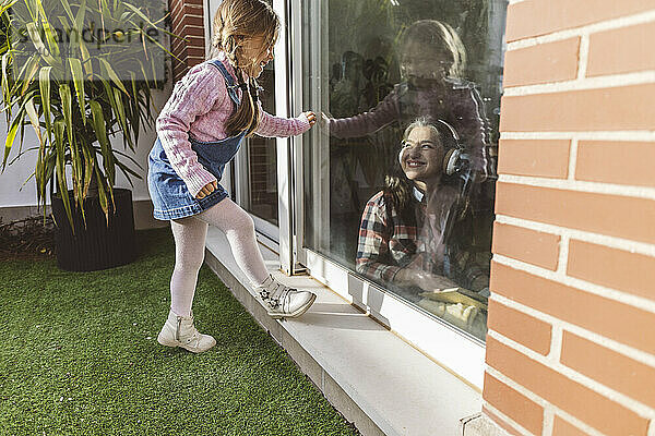 Girl looking at grandmother through window glass