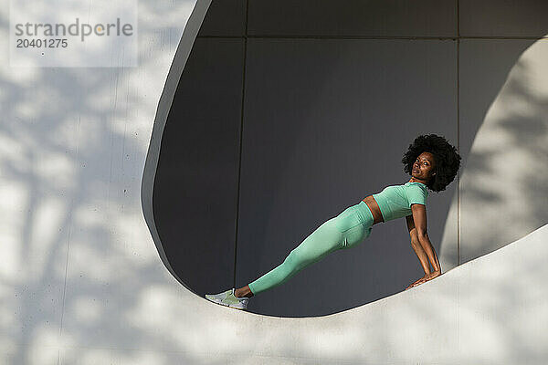 Confident woman with Afro hairstyle balancing on white wall