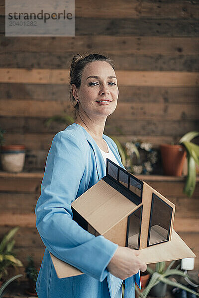 Confident architect carrying model house in office