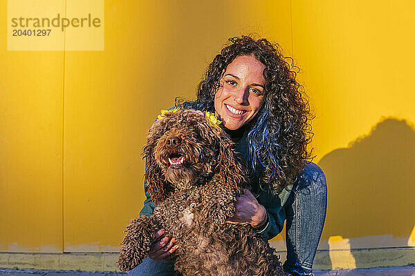 Smiling young woman spending leisure time with water dog in front of yellow wall