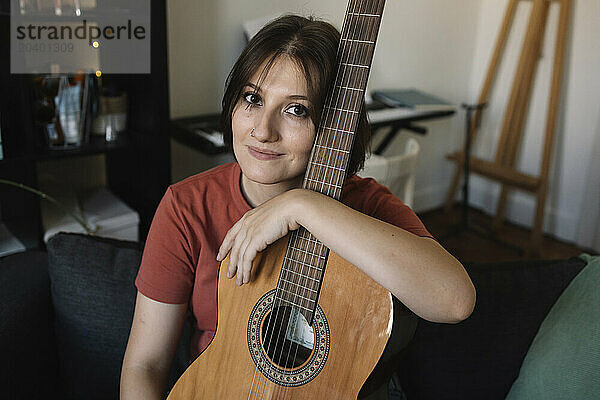 Smiling beautiful woman with acoustic guitar sitting at home