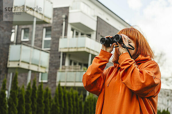 Redhead woman watching through binoculars in front of building