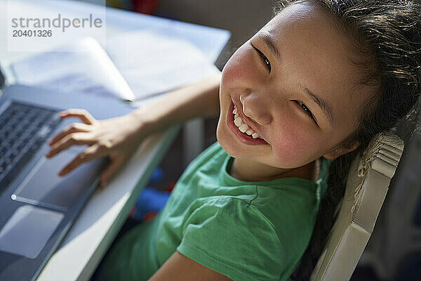 Smiling girl with laptop sitting on chair at home