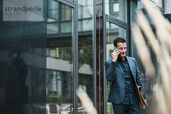 Businessman talking on smart phone near office building