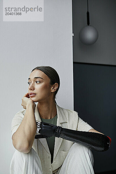 Thoughtful woman with black bionic arm looking away at home