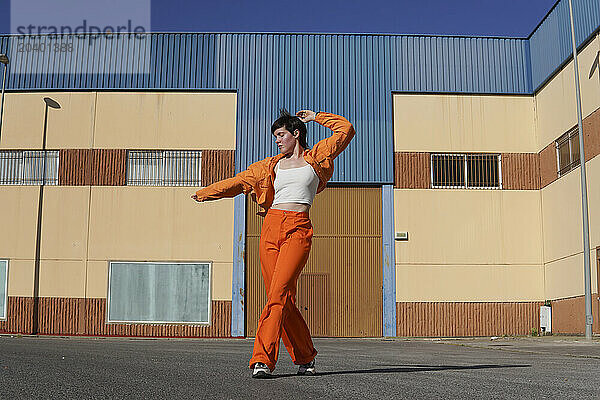 Woman wearing orange casuals dancing in front of building on sunny day