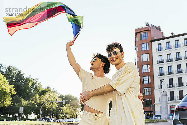 Carefree gay couple waving rainbow flag at gay pride parade