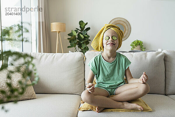 Smiling girl with cucumber slices on eyes sitting at home