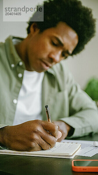 Businessman writing in diary at table working remotely from home office