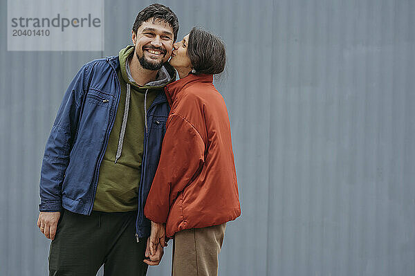 Mature woman kissing man on cheek standing in front of corrugated iron