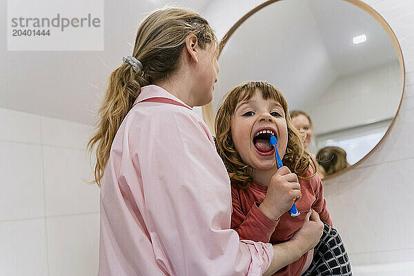 Girl brushing teeth by mother in bathroom