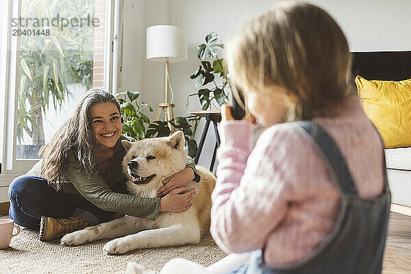 Girl photographing grandmother with dog at home