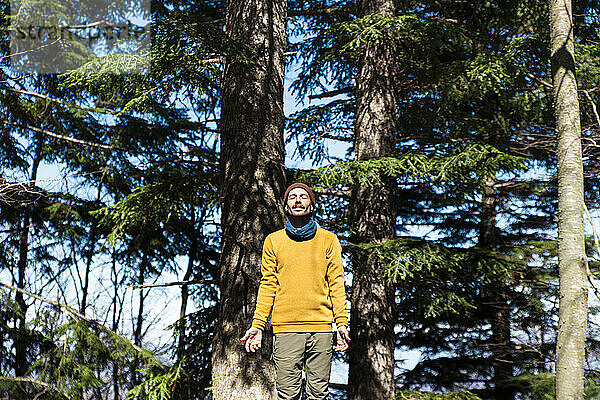 Carefree man standing with eyes closed near trees