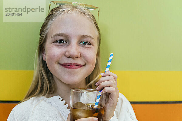 Smiling girl holding glass of cola near colored wall