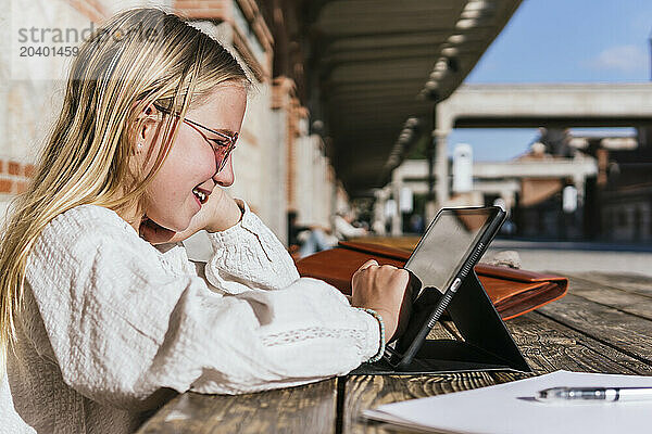 Smiling girl doing E-learning through tablet PC at table