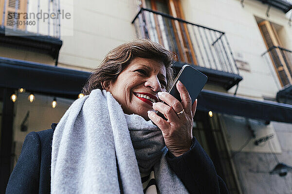 Happy woman talking on smart phone in front of building