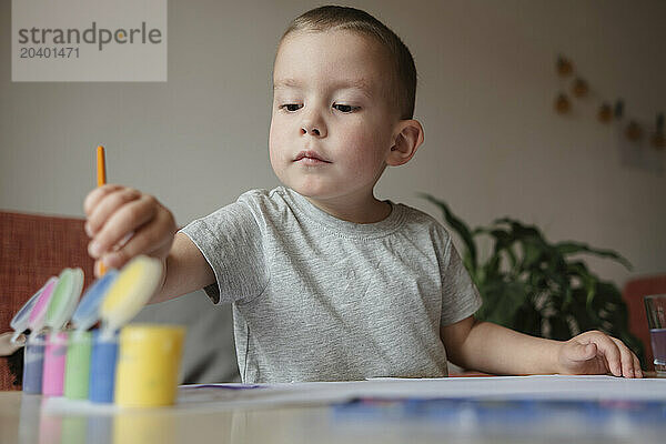 Boy choosing paints on table at home