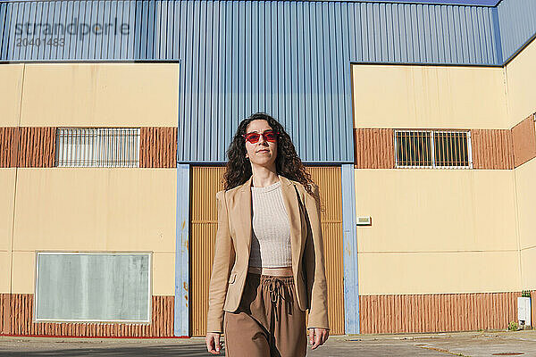 Confident woman with red sunglasses walking in front of building