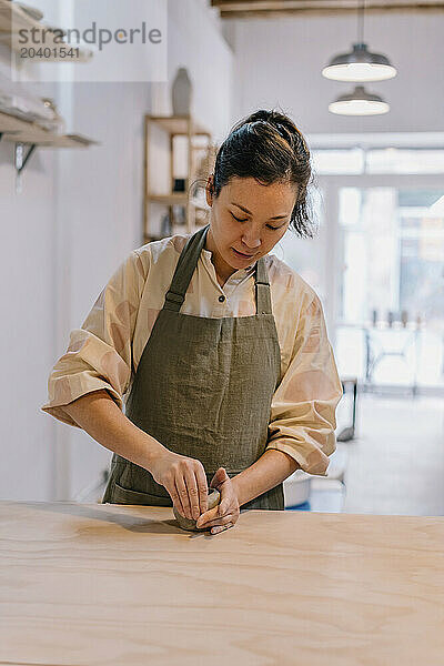 Skilled artist molding clay standing by table at pottery workplace