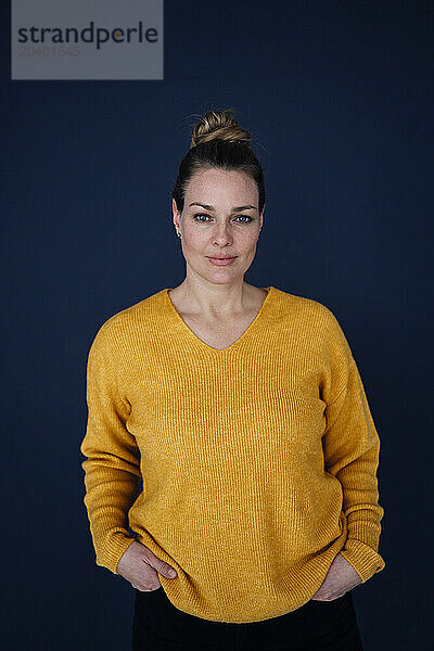 Confident beautiful woman standing with hands in pockets against colored background