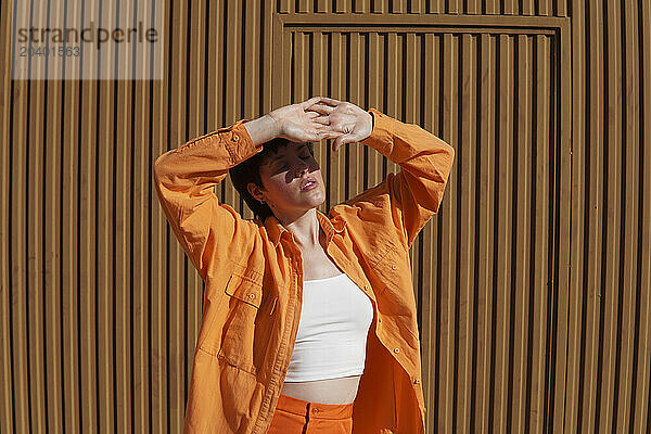 Woman shielding closed eyes with hands standing in front of brown wall