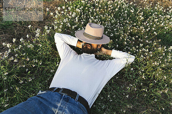 Man covering face with hat and lying on flowering plants