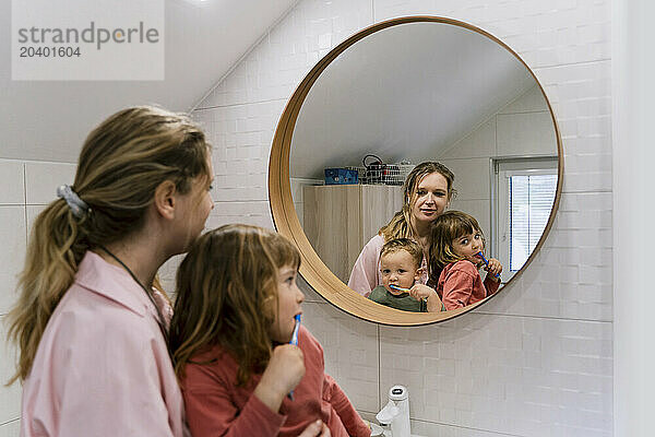 Mother with children brushing teeth in bathroom