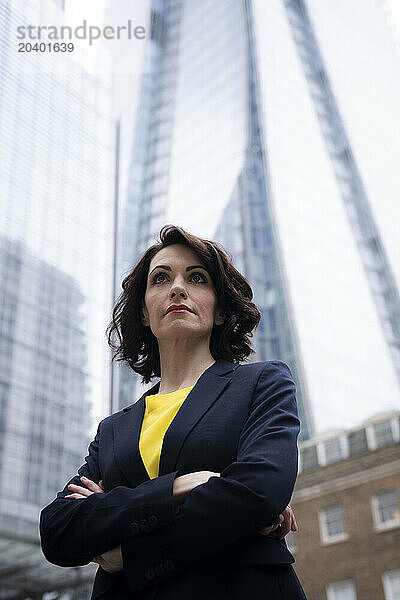 Confident businesswoman standing with arms crossed in front of skyscraper