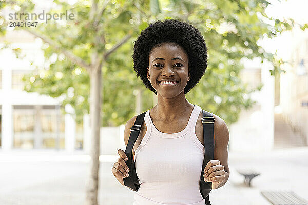 Smiling Afro woman holding straps of backpack